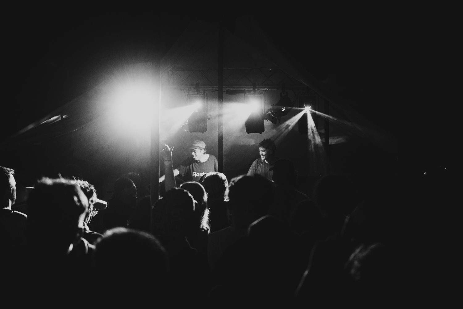 Black and white photo of live music performance with crowd and dramatic stage lighting.