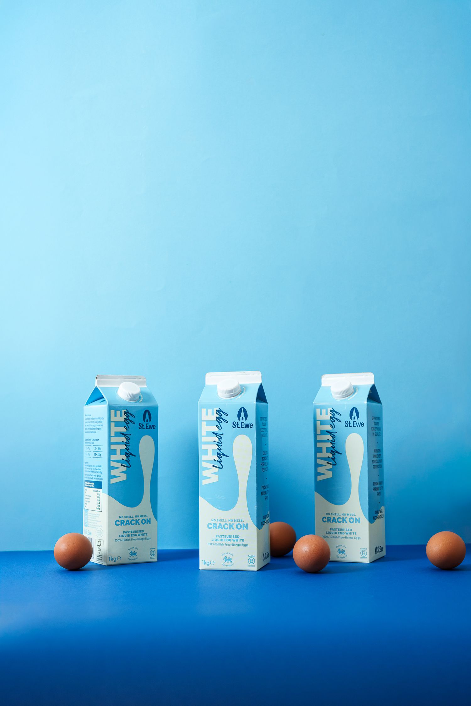 Three white cartons of liquid egg whites with brown eggs on blue background.