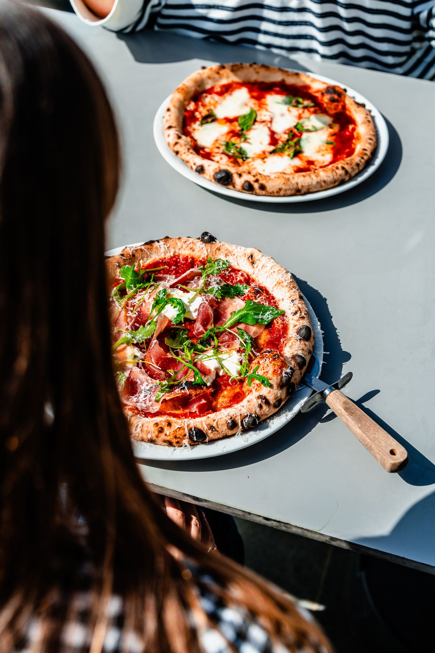 Overhead view of two Neapolitan pizzas with prosciutto, arugula, and fresh mozzarella.