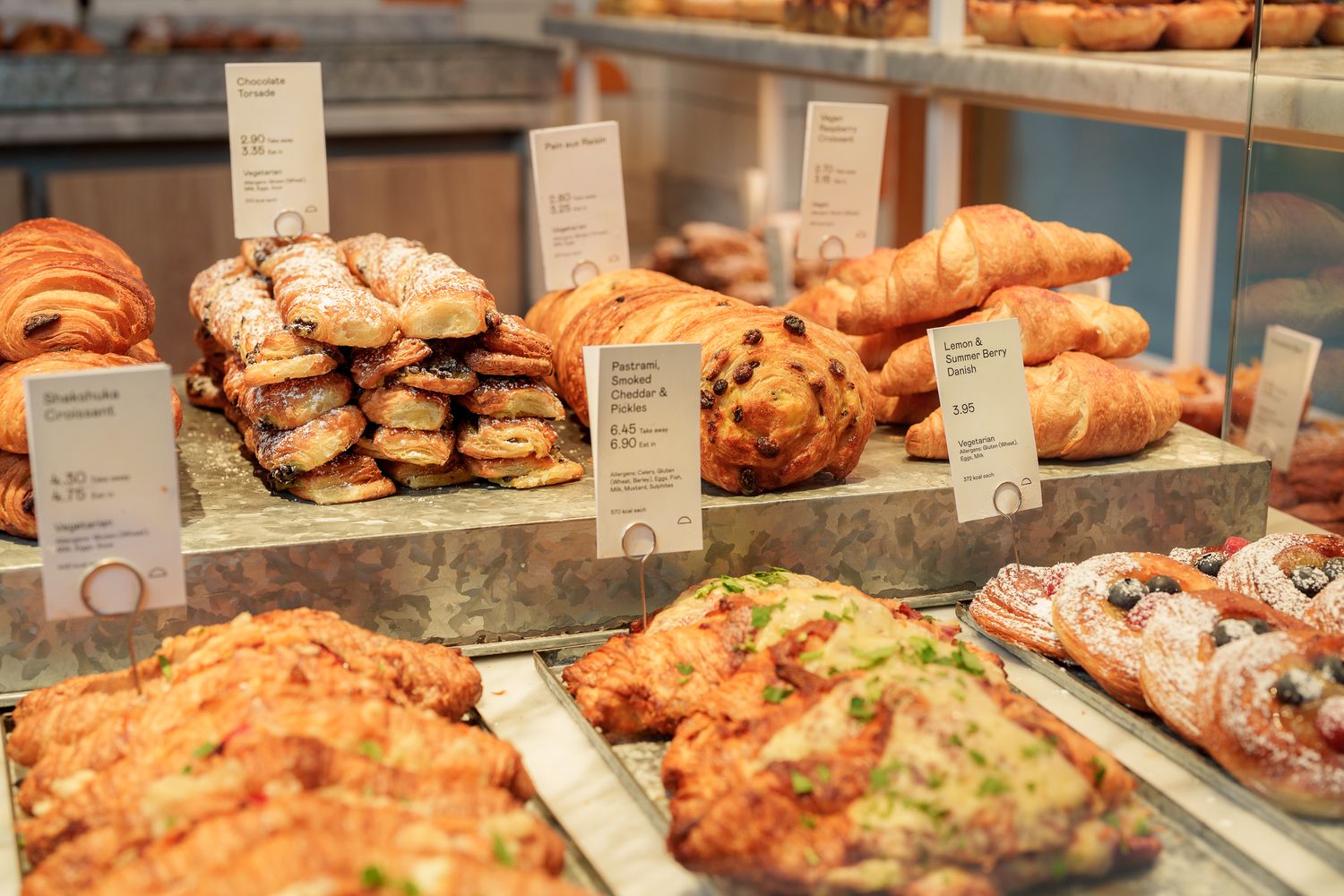 Bakery display case filled with fresh croissants, pastries, and assorted baked goods with labels.