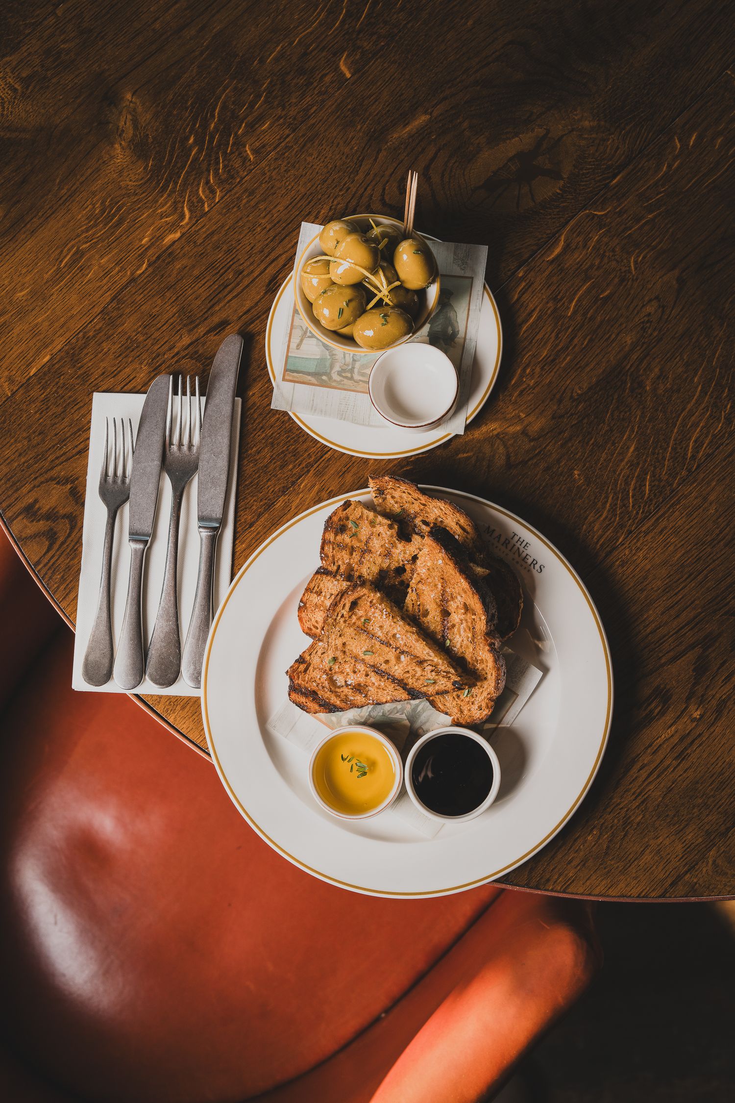 Overhead view of crispy fried chicken with dipping sauces, olives, and silverware on wooden table.