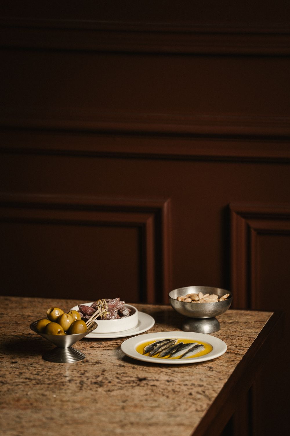 Spanish tapas with olives, anchovies in oil, and nuts on a marble bar counter.