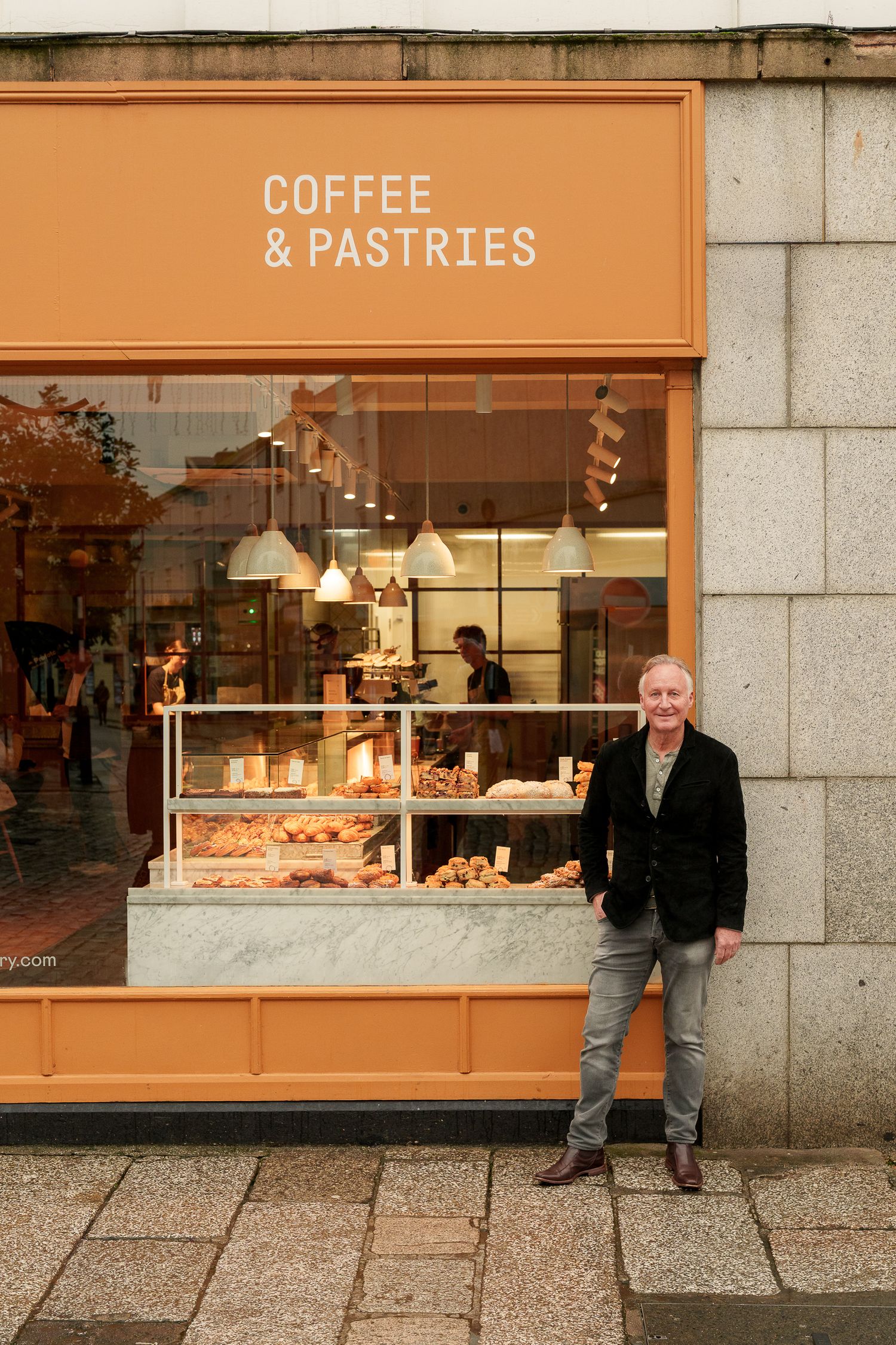 Man standing outside a coffee and pastries shop with an orange storefront display window.
