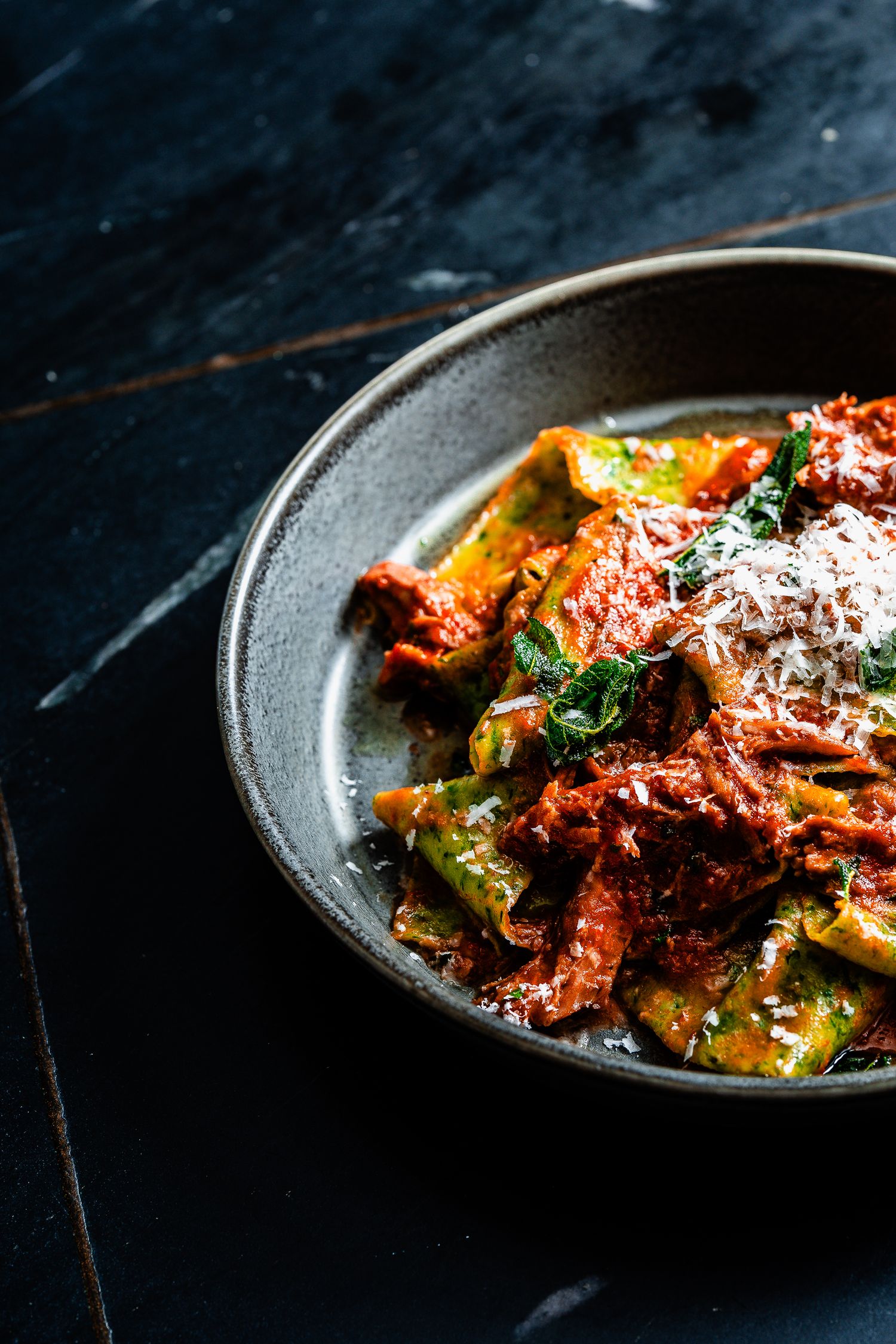 Rustic bowl of pappardelle pasta with slow-cooked tomato ragu, fresh herbs, and grated parmesan cheese.