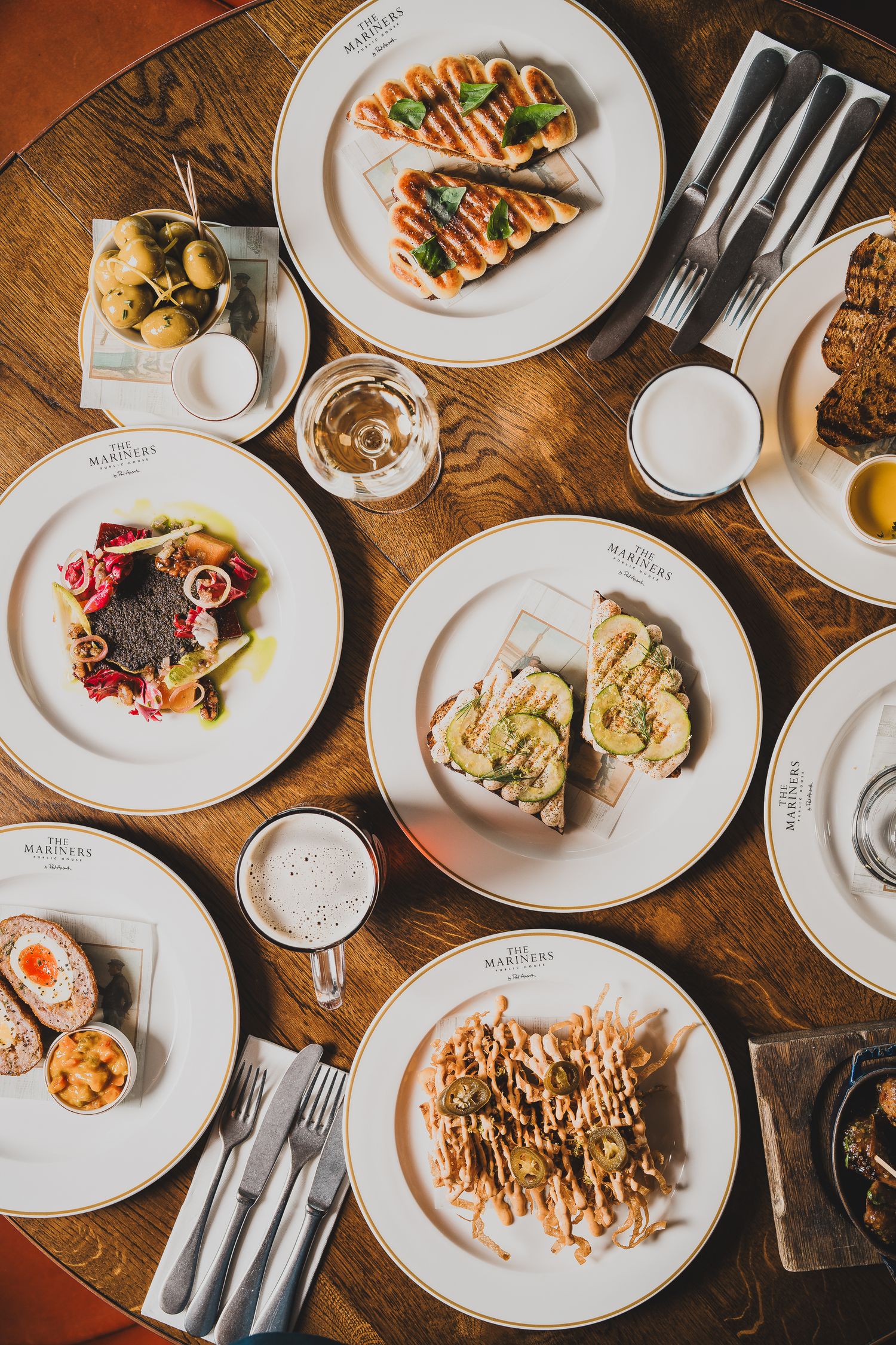 Overhead view of multiple dishes on white branded plates spread across a wooden restaurant table.