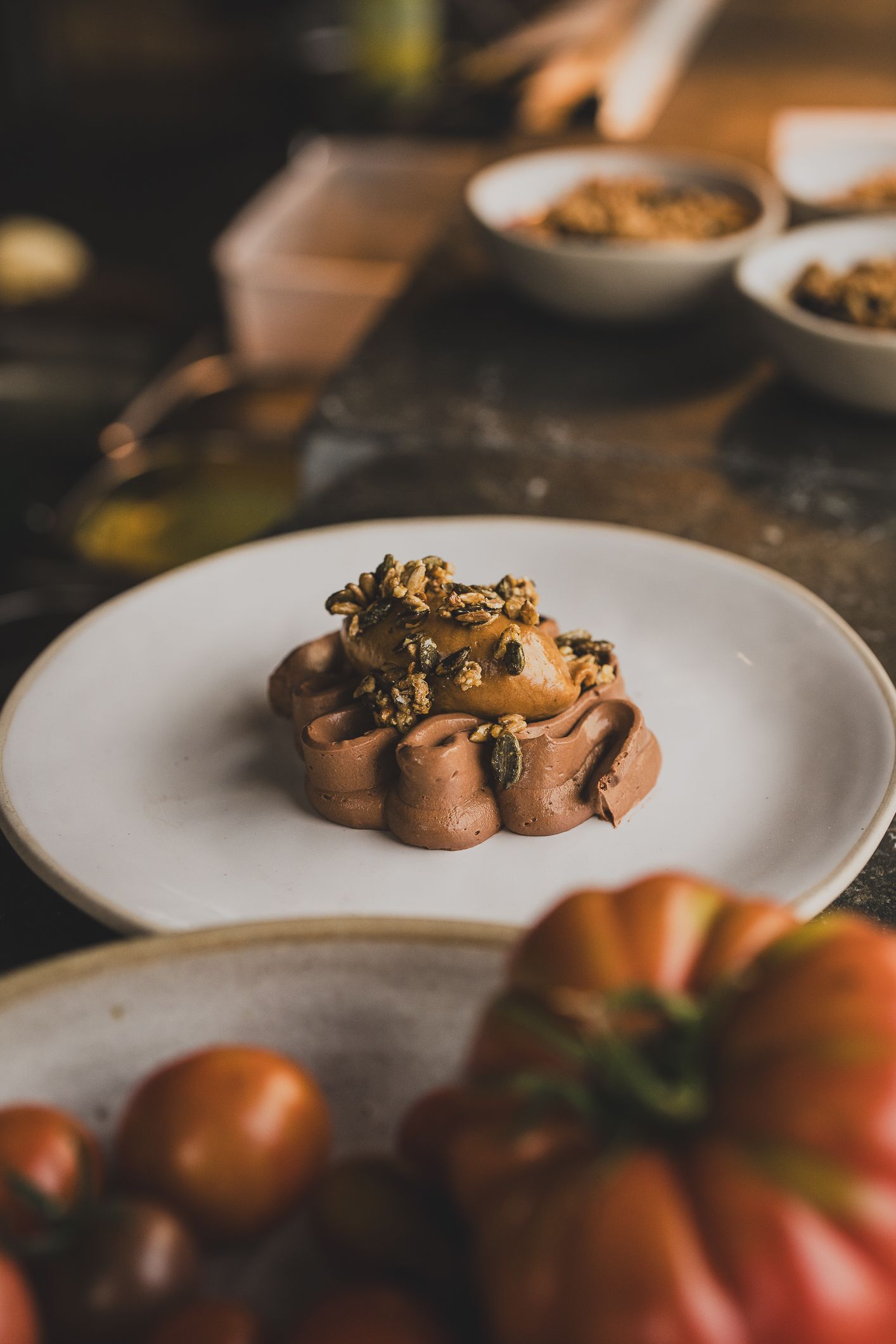 Elegant plated chocolate dessert topped with caramelized nuts on a white ceramic plate in a rustic kitchen.
