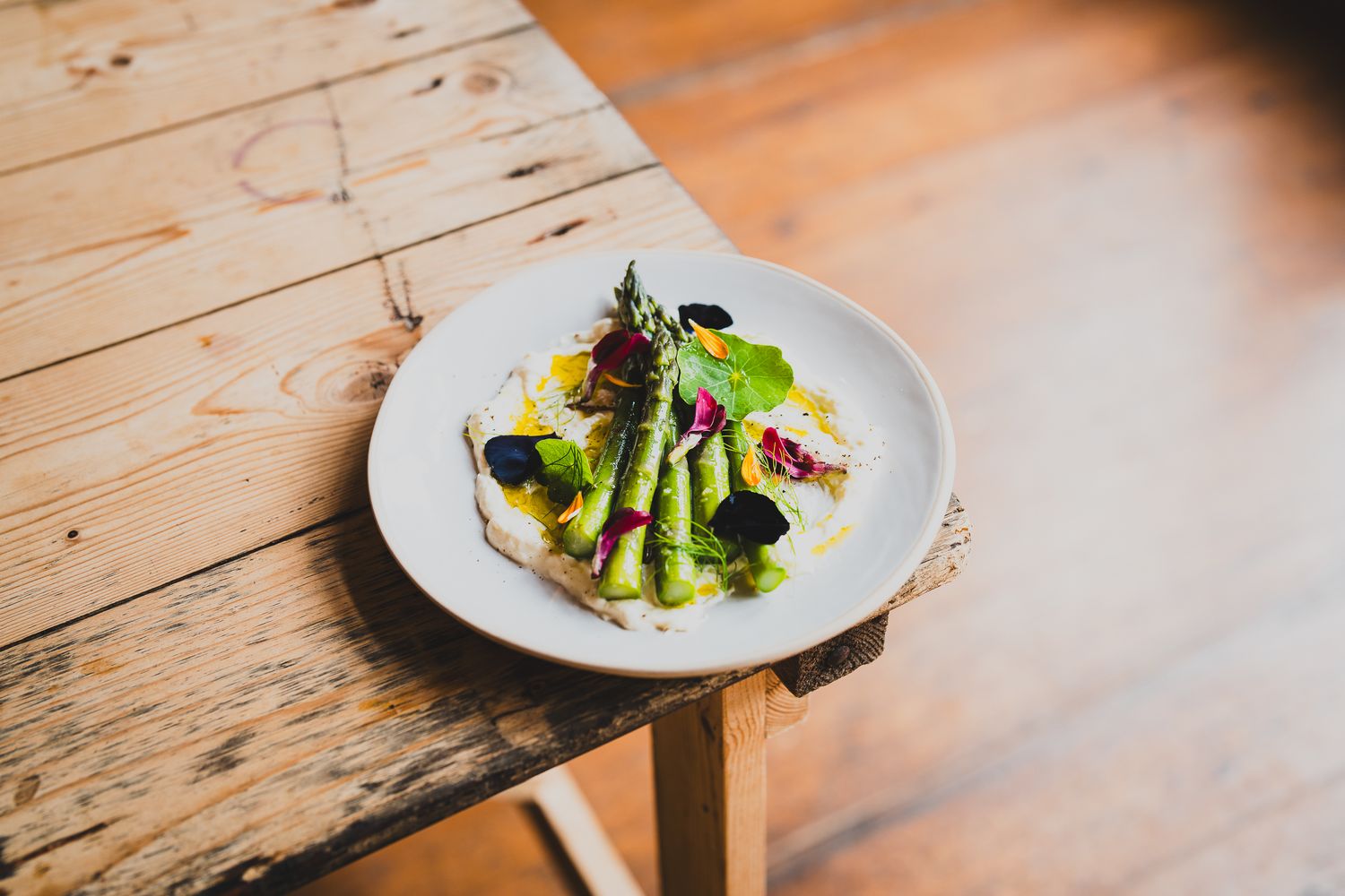 Asparagus salad with edible flowers on a white plate on a wooden surface.