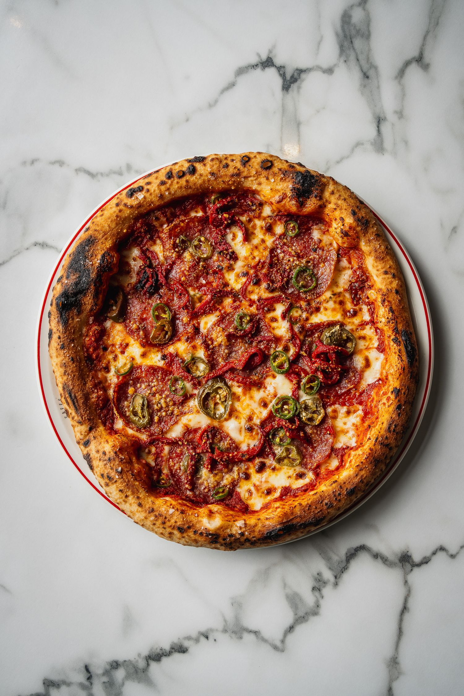 Neapolitan pepperoni pizza with jalapenos on a marble surface with charred crispy crust.