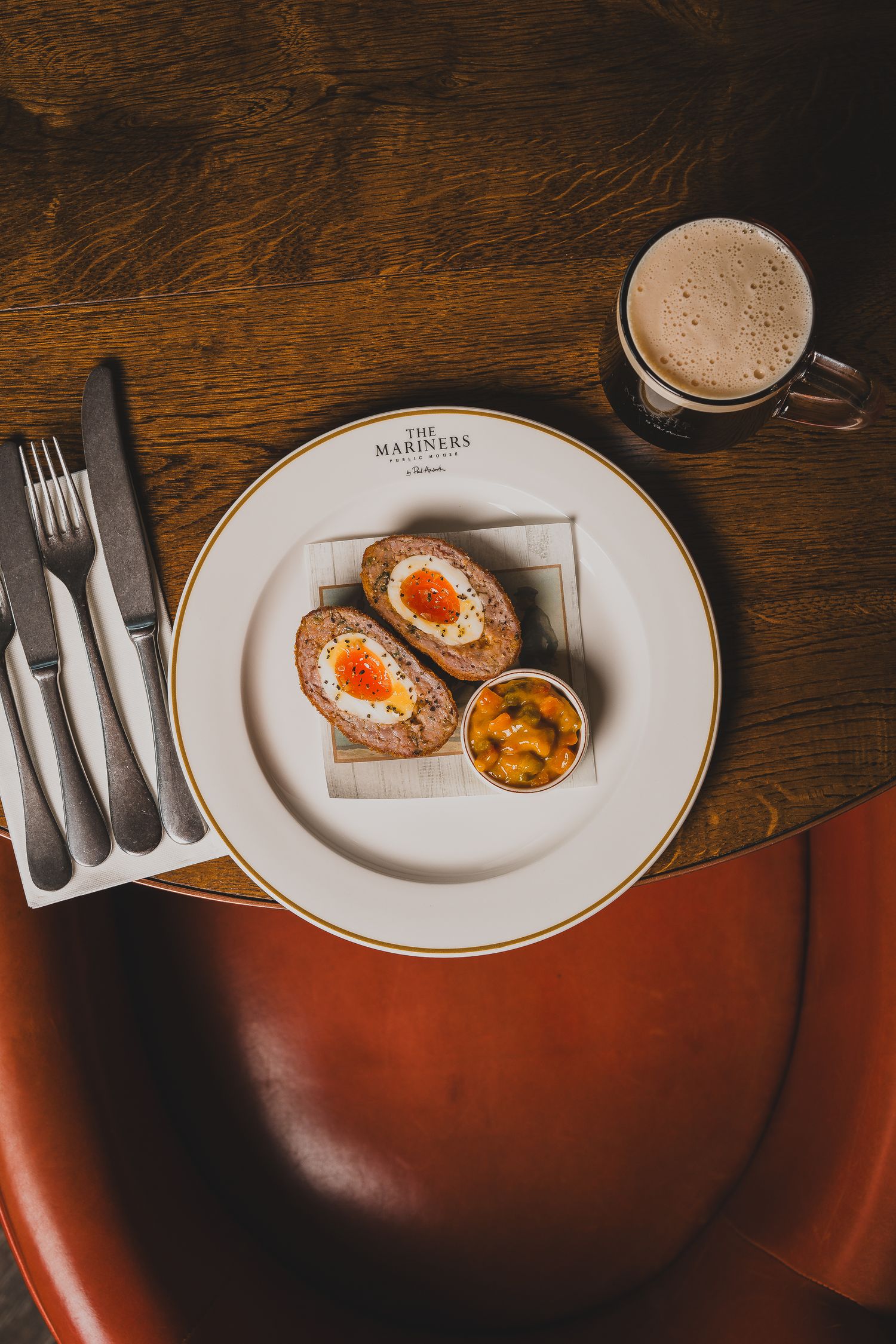Scotch egg with mustard dipping sauce on branded plate beside a frothy coffee mug.