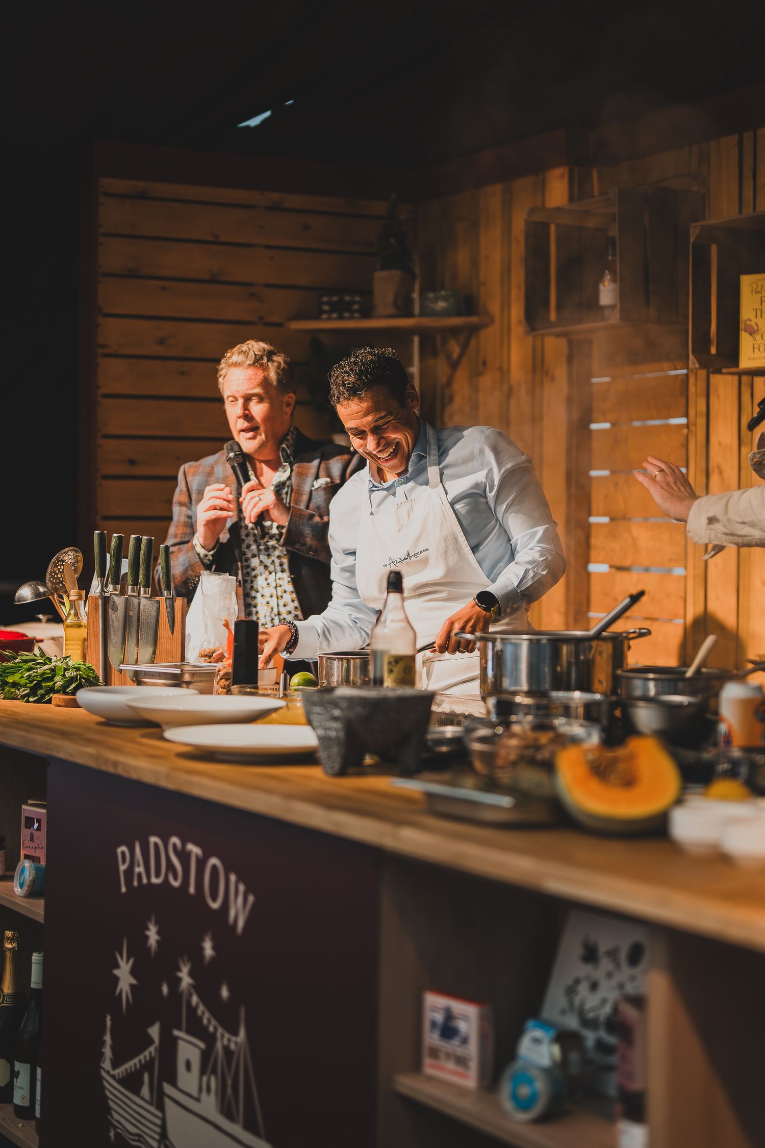 Two chefs cook and laugh together at the Padstow food festival kitchen demonstration.