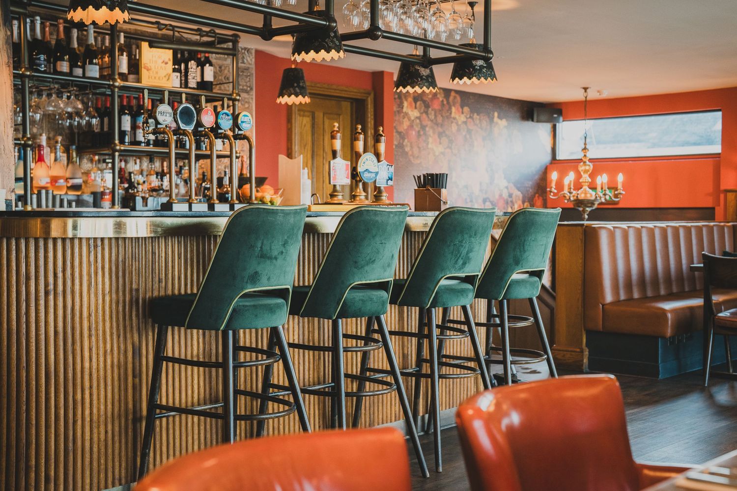 Stylish bar interior with green velvet stools, wood paneling, and red booth seating.