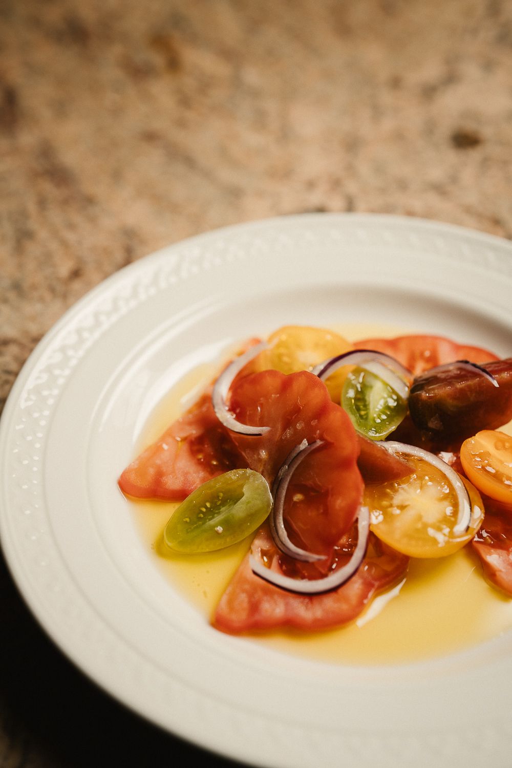 Colorful heirloom tomato salad with red onion slices in golden dressing on white plate.