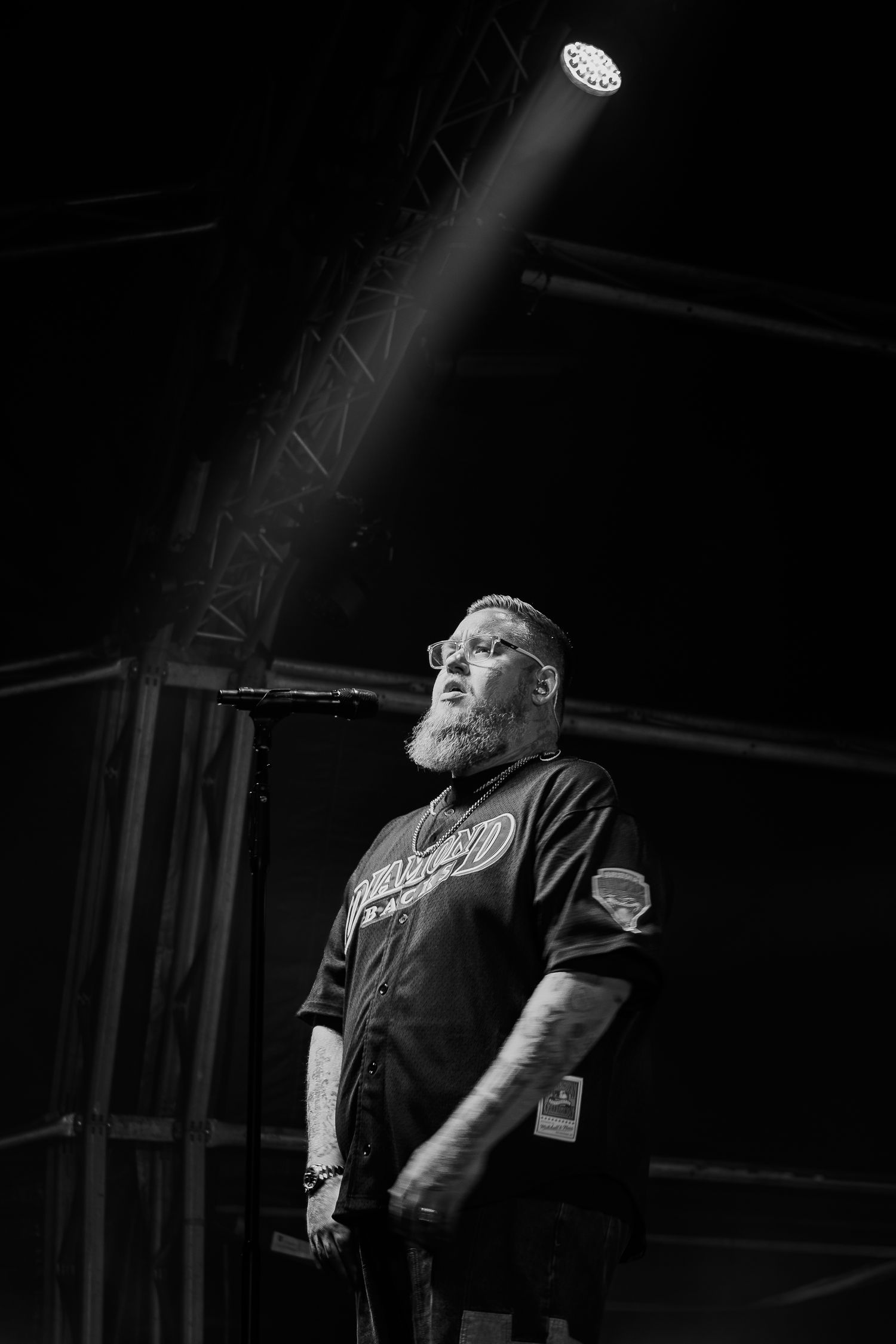 Black and white portrait of a bearded man on stage under a single spotlight.