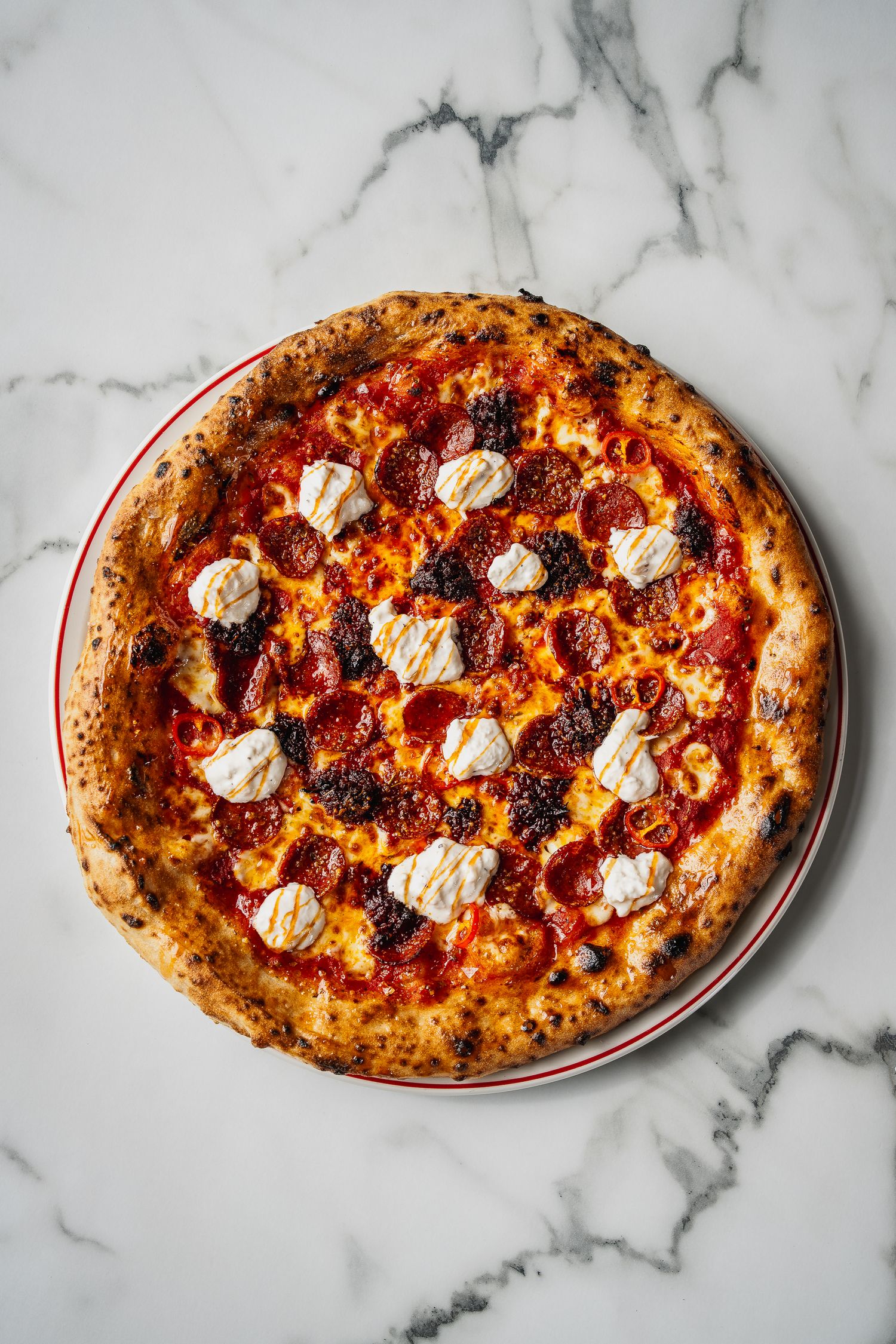 Overhead view of Neapolitan pepperoni pizza with burrata cheese on marble surface.