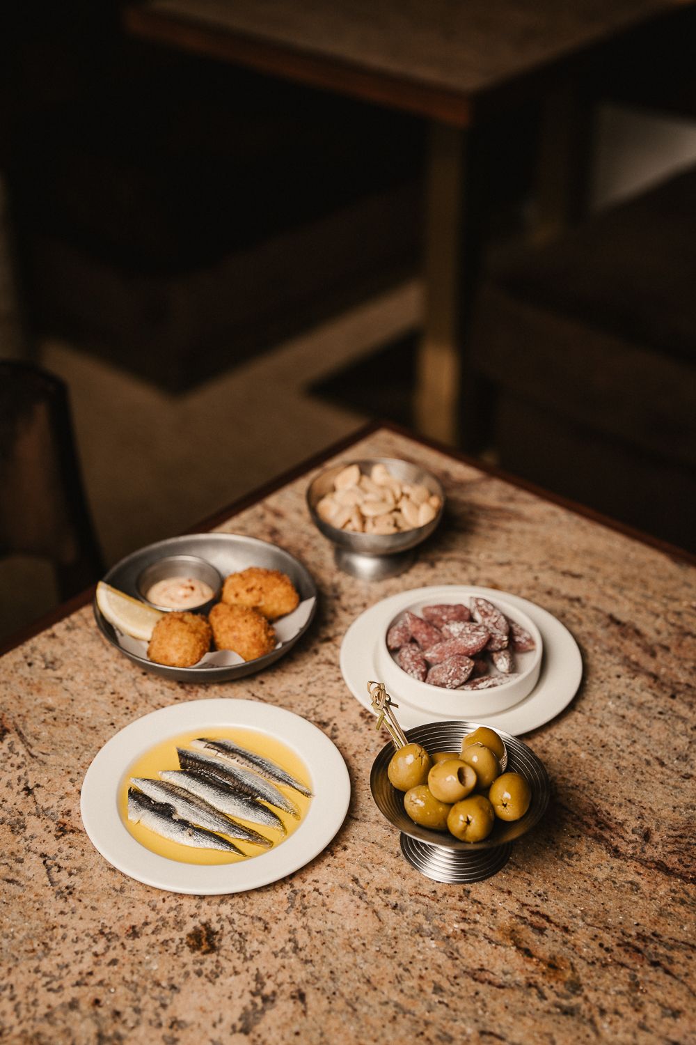 Spread of Spanish tapas including anchovies, olives, croquetas and charcuterie on marble bar.