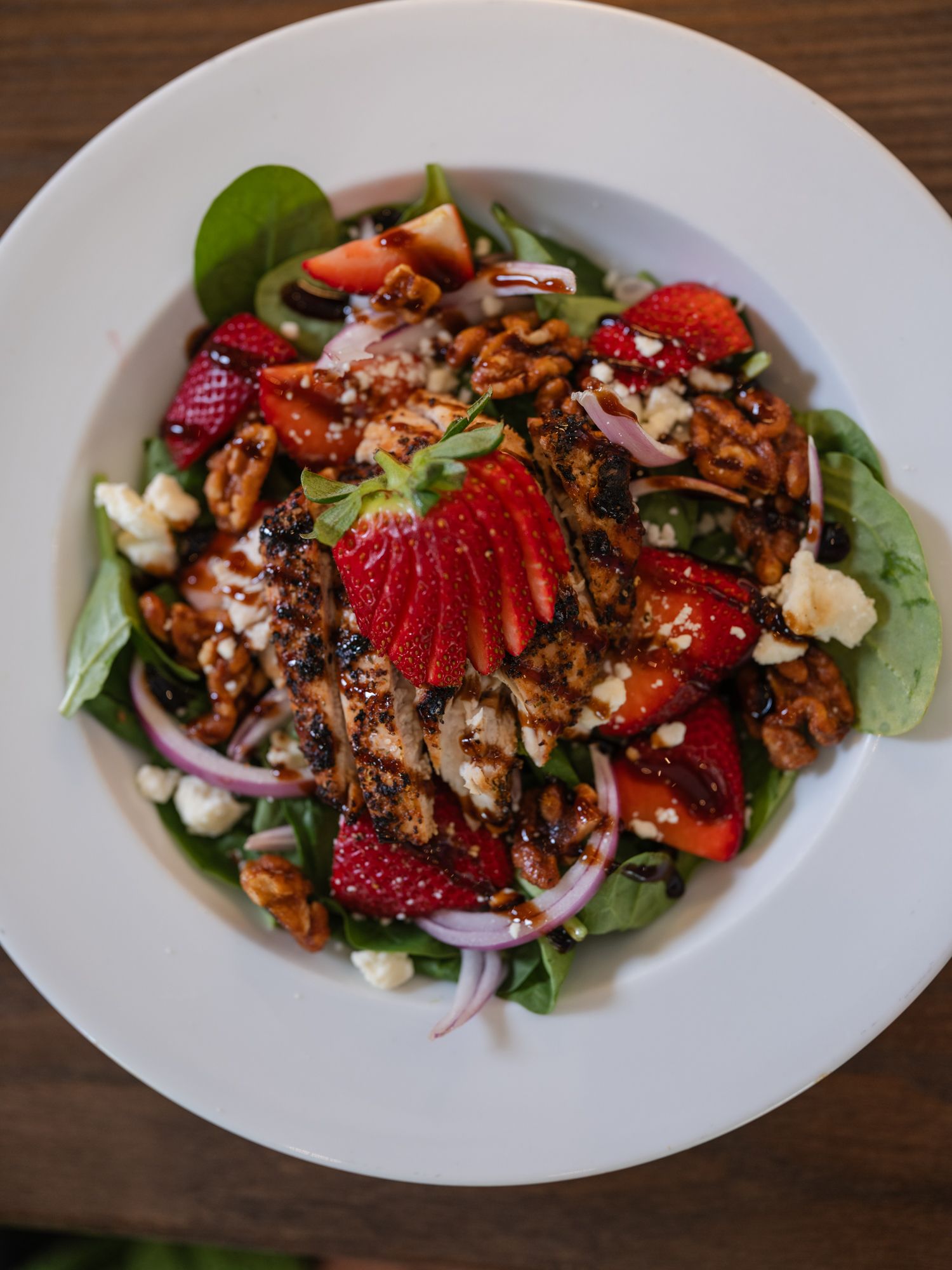 Fresh spinach salad topped with grilled chicken, sliced strawberries, candied pecans, red onion, and balsamic dressing.