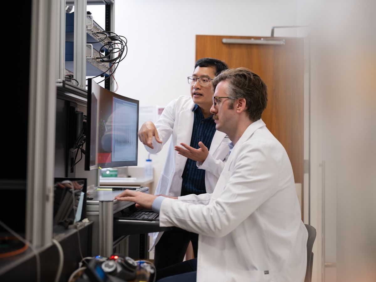 Two researchers in white lab coats reviewing data on computer monitors in a medical laboratory.