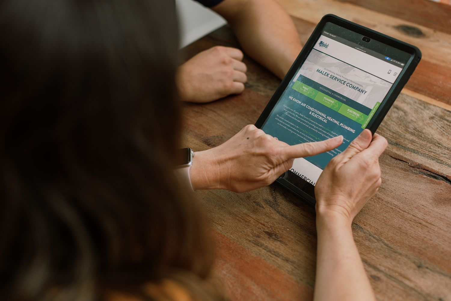 Two people collaborate on a tablet displaying a website at a wooden table.
