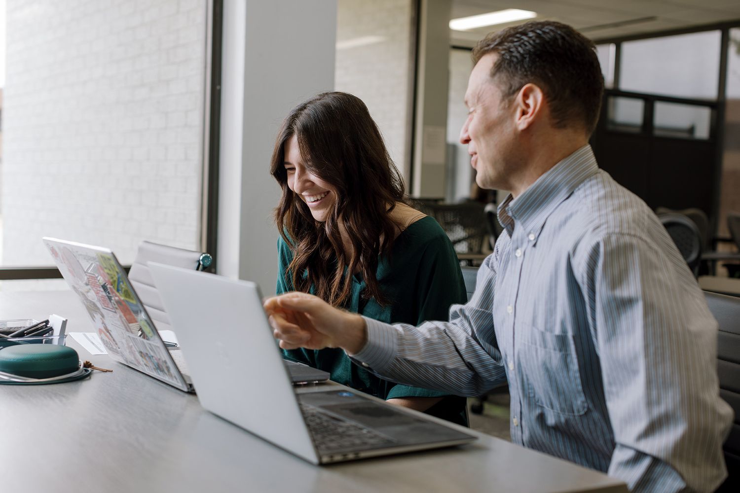 Two professionals smiling and collaborating on a laptop in a bright modern office workspace.