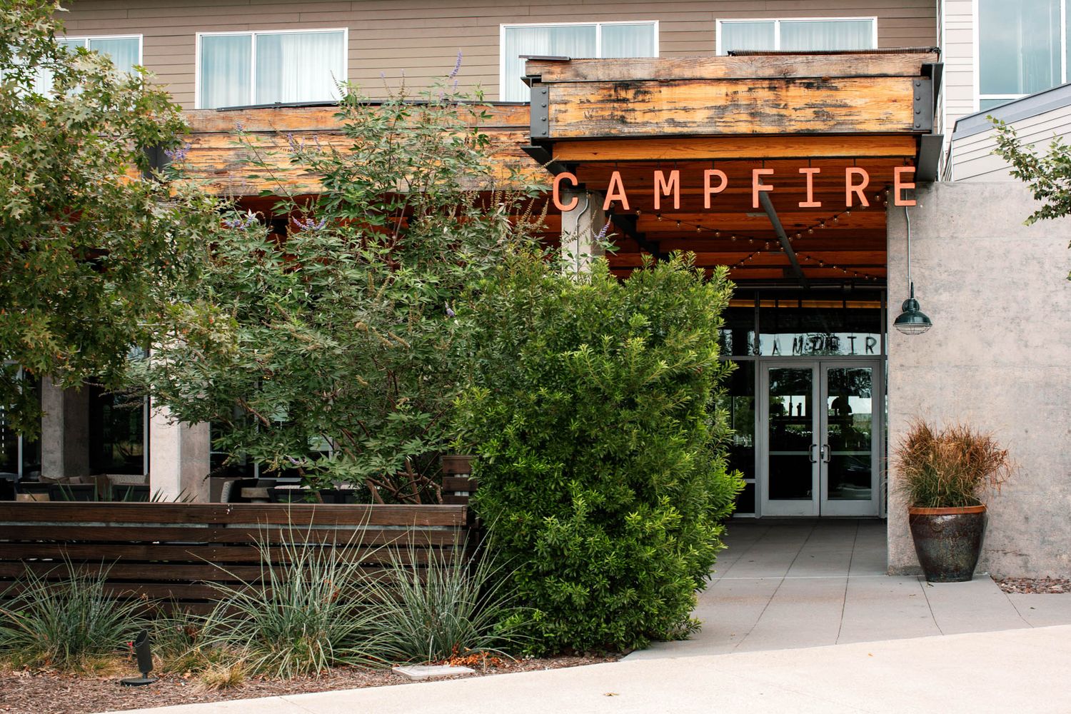 Campfire restaurant exterior featuring rustic wood signage surrounded by lush greenery and modern architecture.