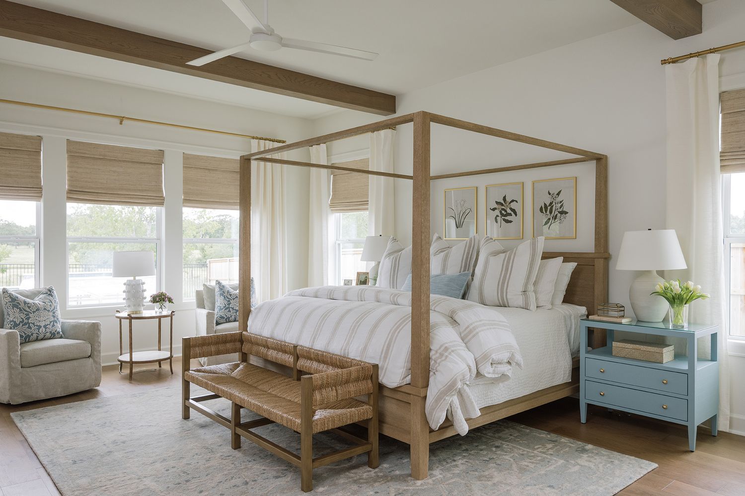 Elegant four-poster canopy bed in neutral tones with white bedding, blue nightstands, and natural wood bench in bright bedroom.