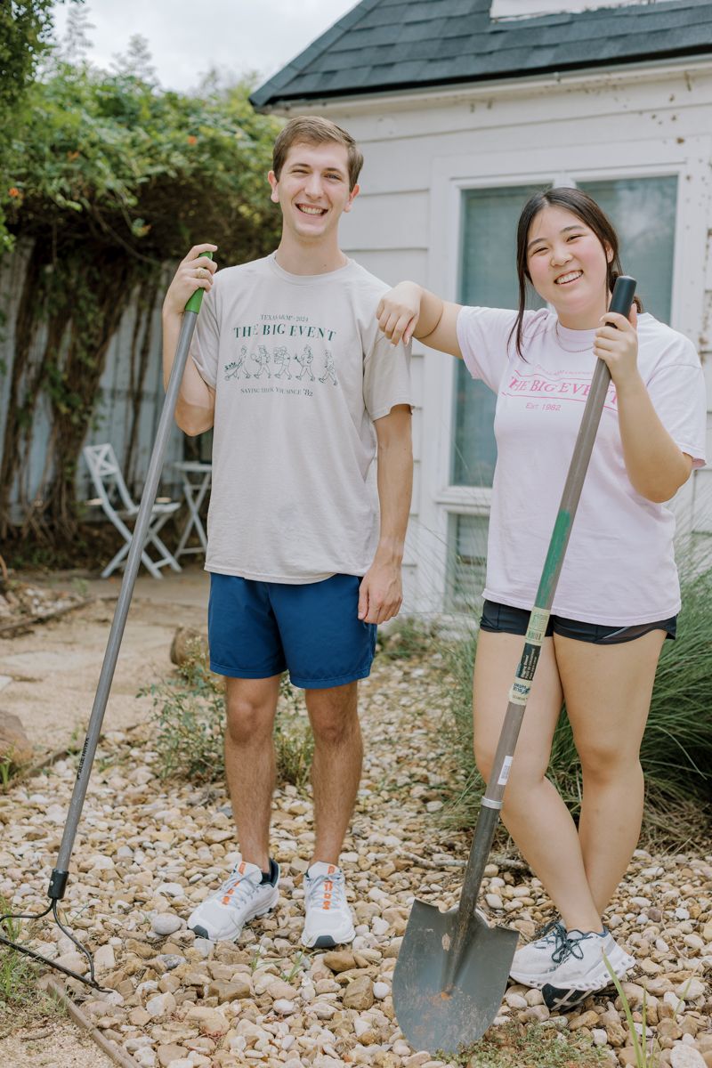Two smiling students holding gardening tools including a rake and shovel while volunteering at The Big Event service day.