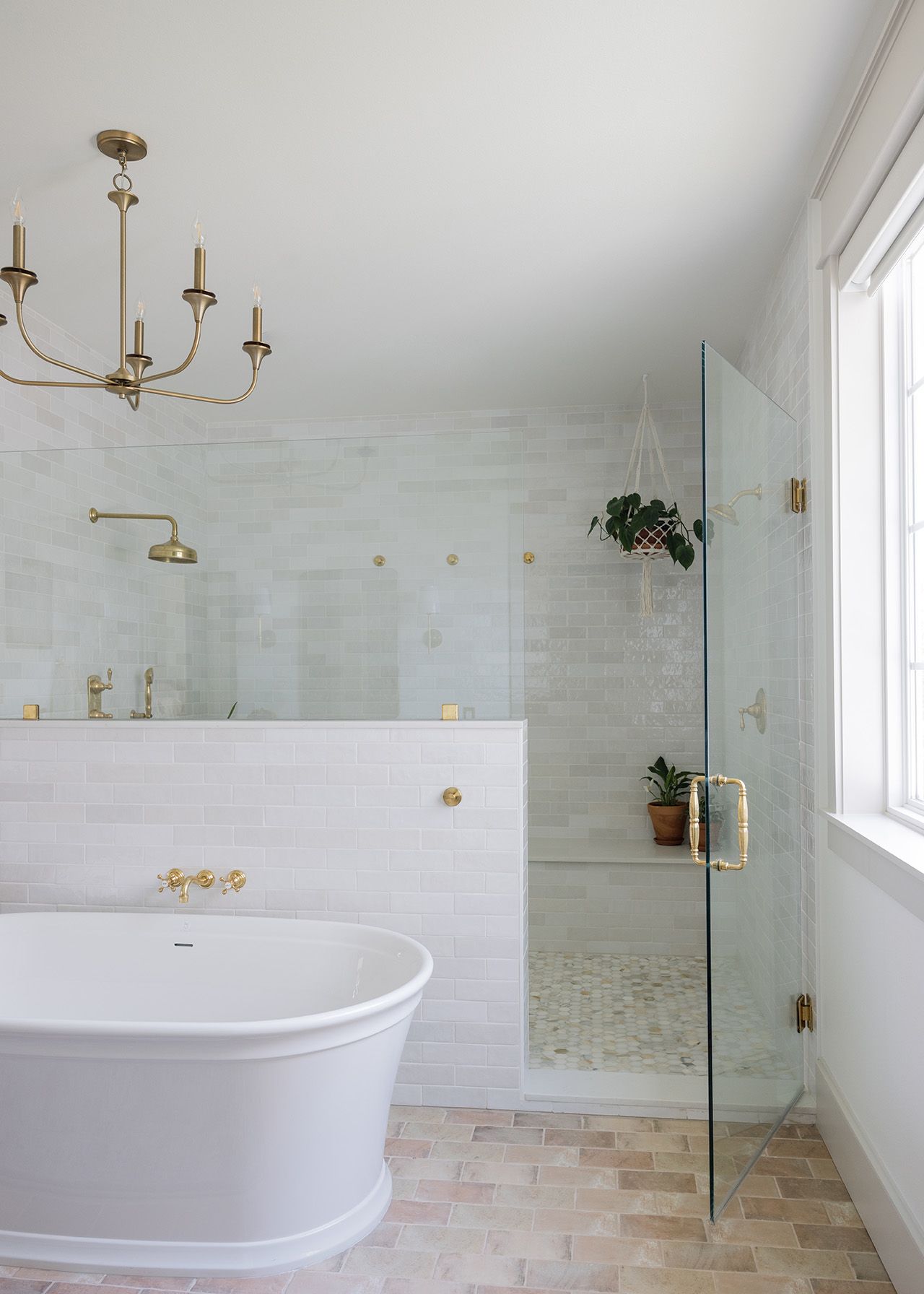 Elegant white bathroom with freestanding tub, glass shower, gold fixtures, and brass chandelier.