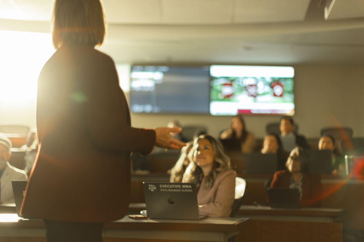 Female instructor presenting to students in a modern university classroom with digital display screens.
