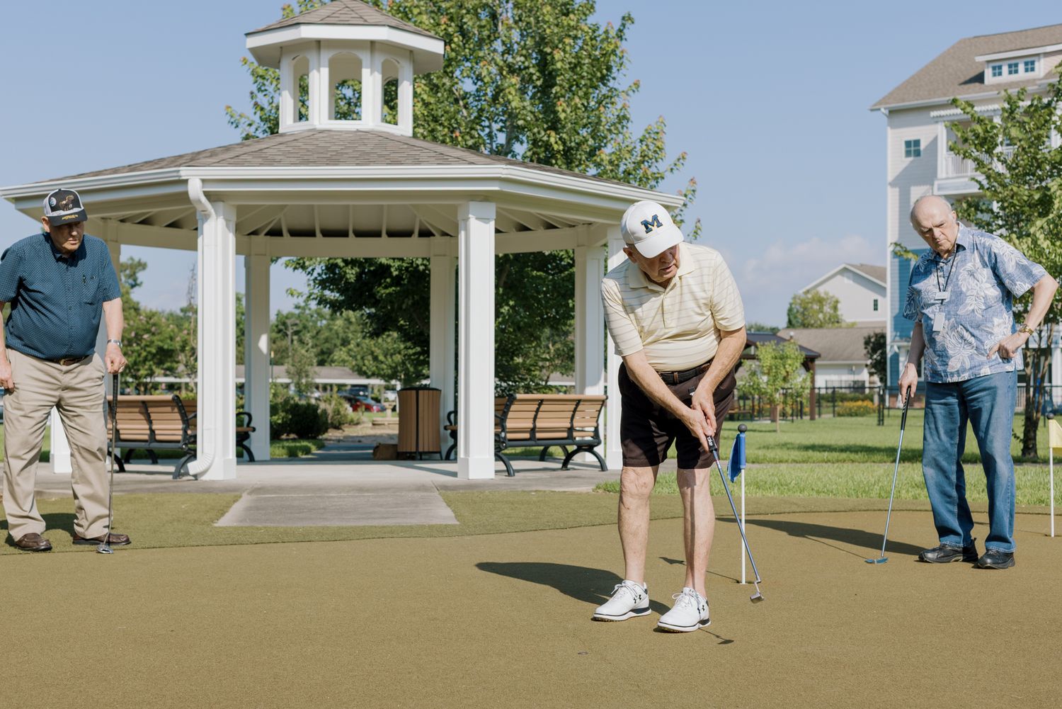 Seniors enjoying a game of mini golf near a white gazebo on a sunny day at a retirement community.