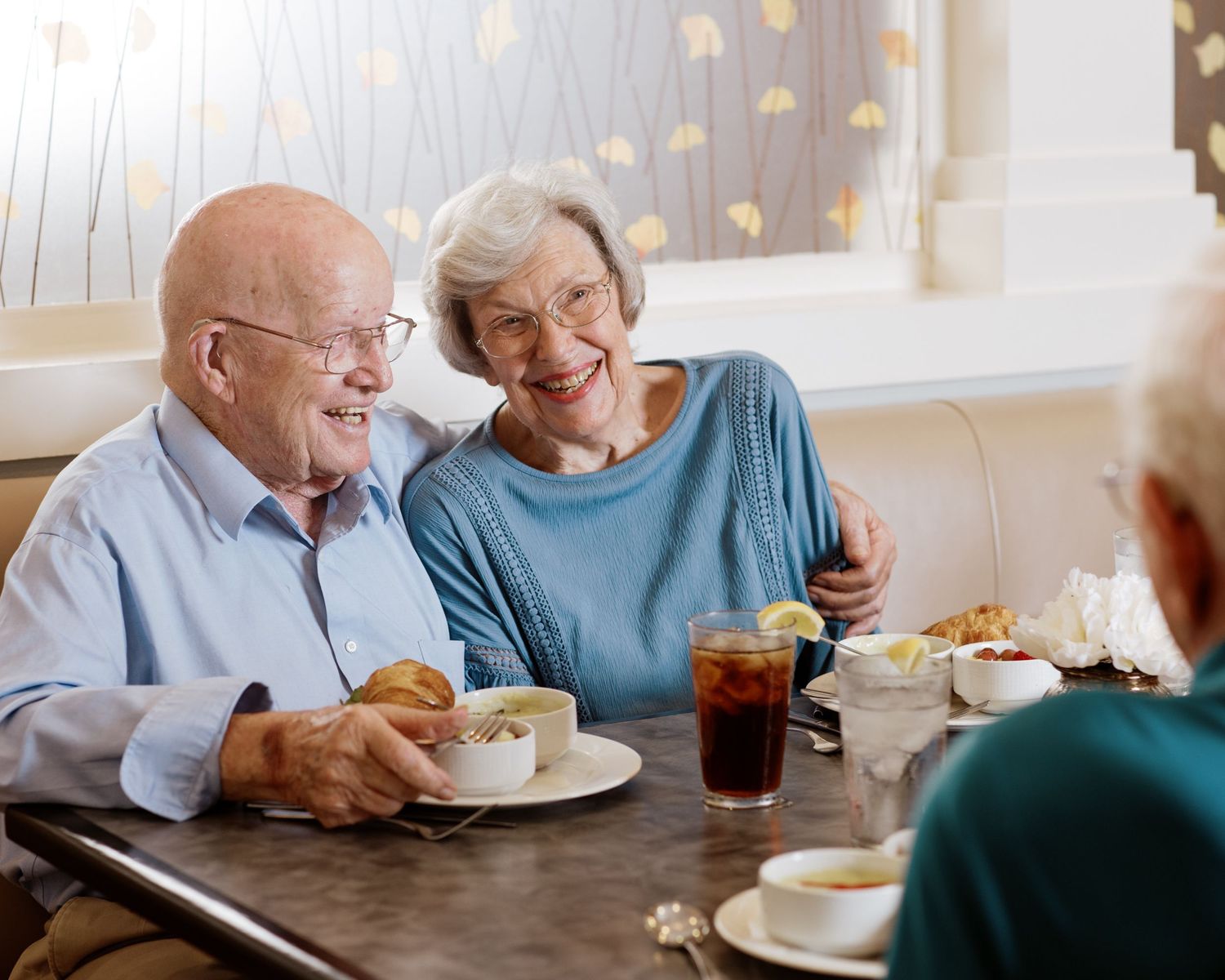 Happy elderly couple sharing a meal and laughing together at a restaurant booth.