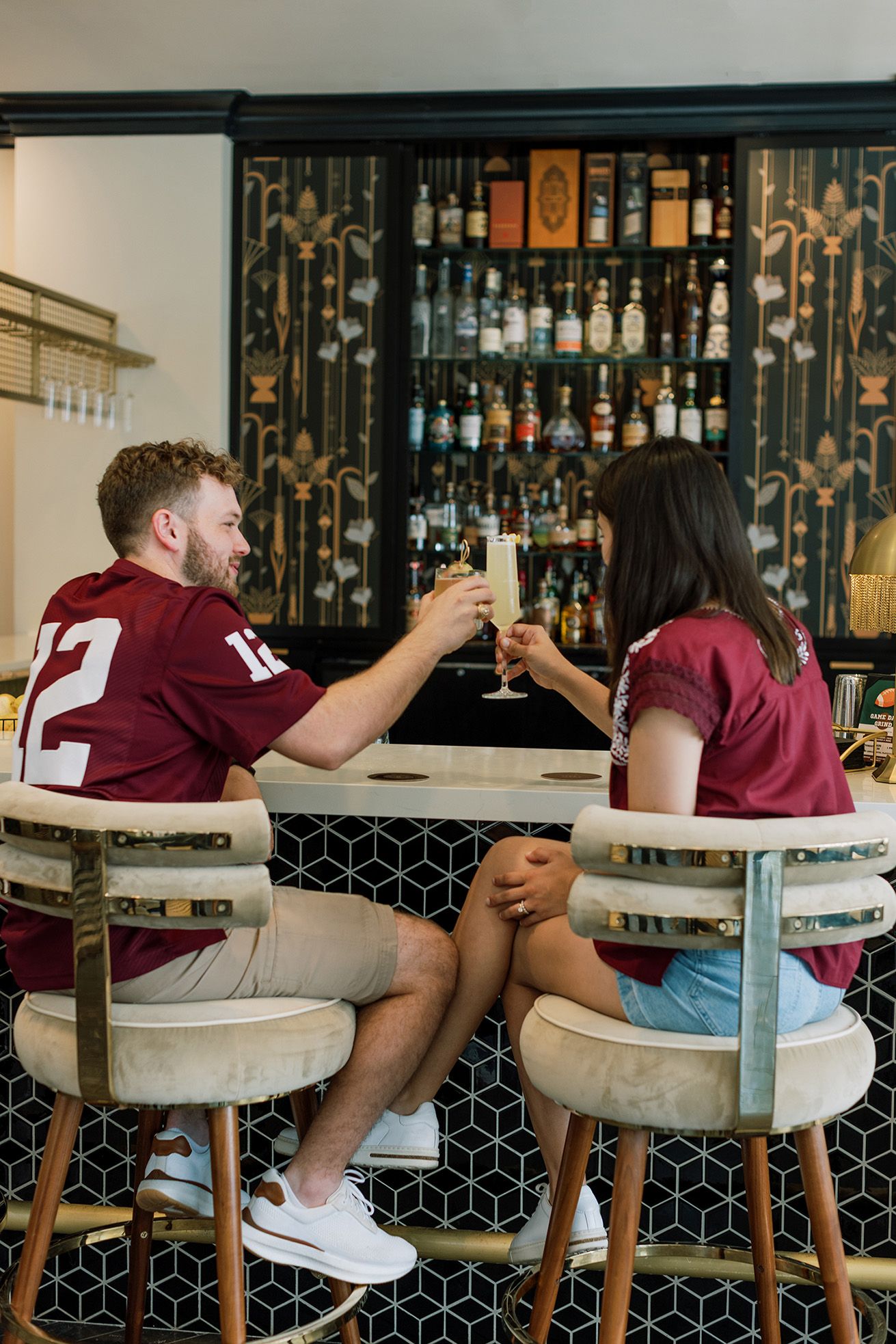 Couple in matching maroon jerseys toasting champagne glasses at an elegant bar.