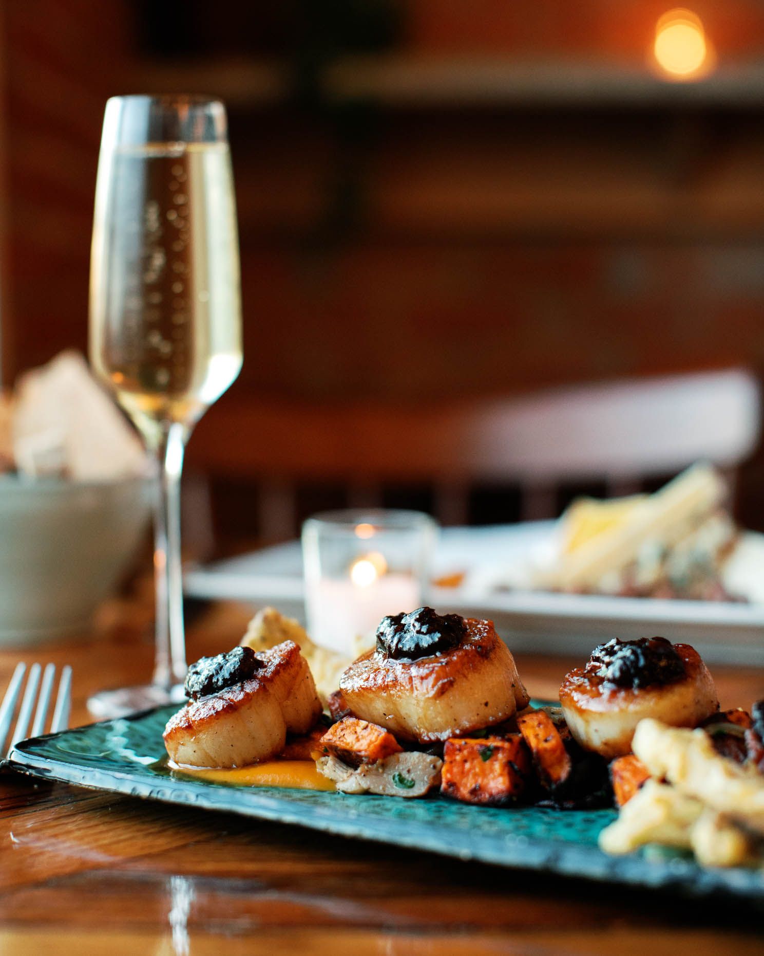Seared scallops topped with caviar served on a teal plate with champagne and candlelight in background.