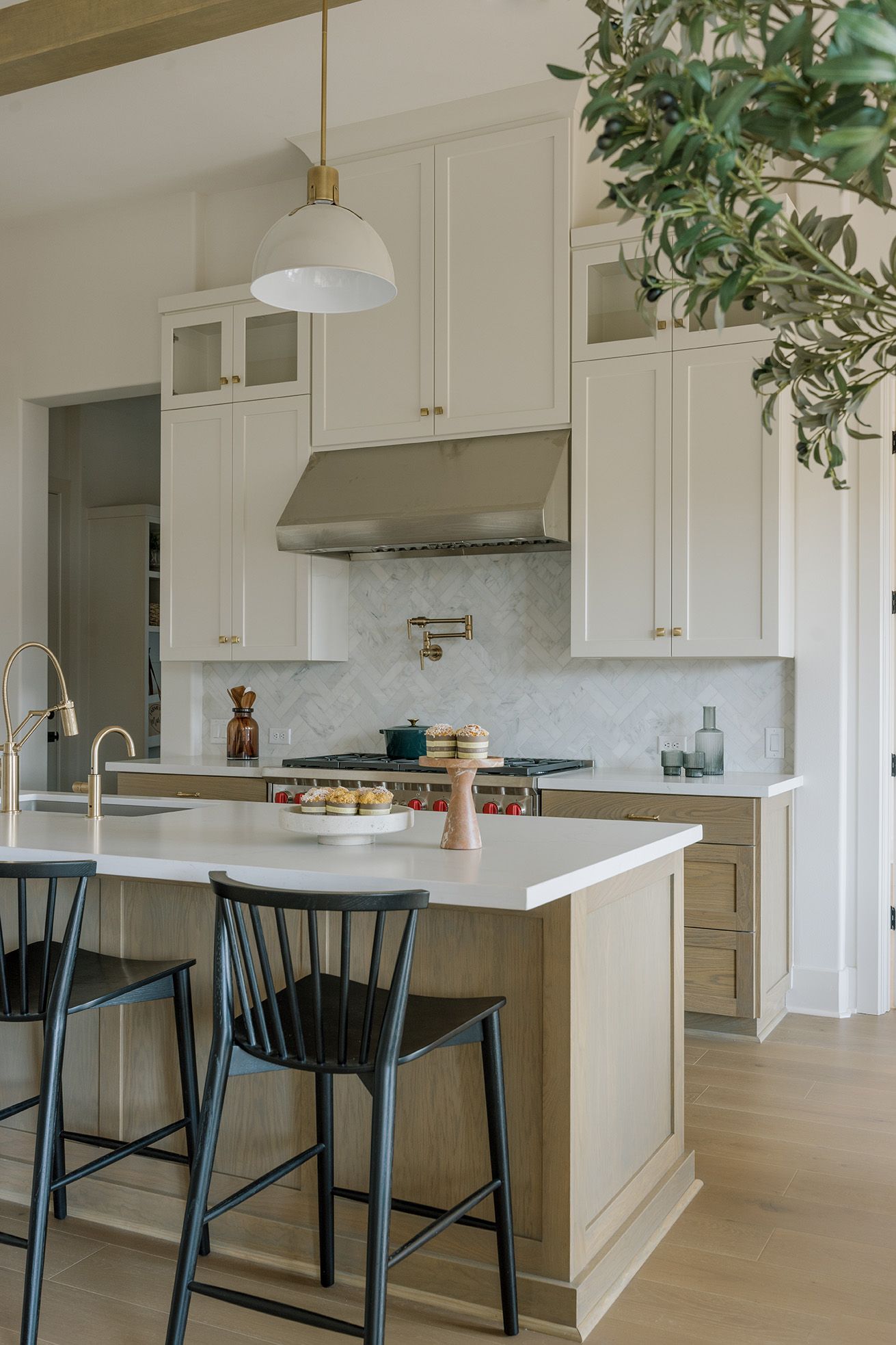 Bright kitchen with cream shaker cabinets, wood island, black Windsor barstools, herringbone tile backsplash, brass hardware.