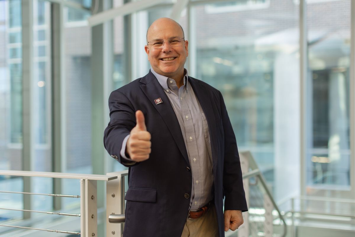 Cheerful businessman in navy blazer giving thumbs up in a bright modern office building.