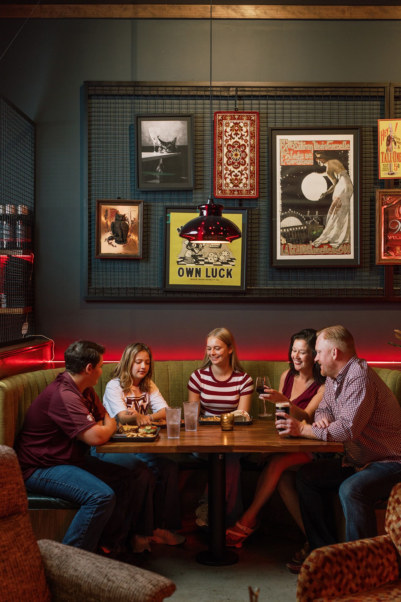 Group of five friends laughing and dining together in a cozy bar with eclectic wall art.