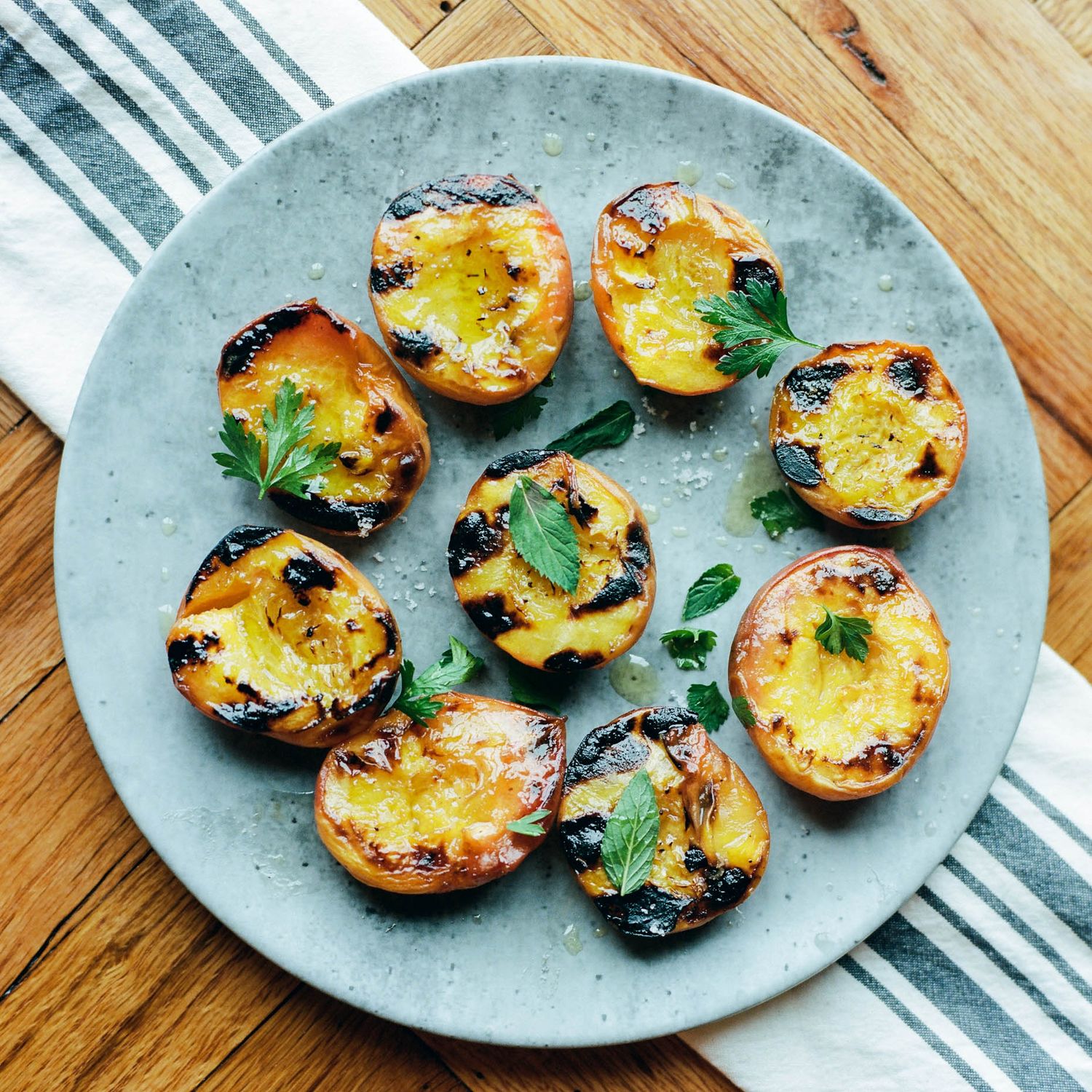 Grilled peach halves with char marks, garnished with fresh herbs on a rustic gray plate atop a wooden table.