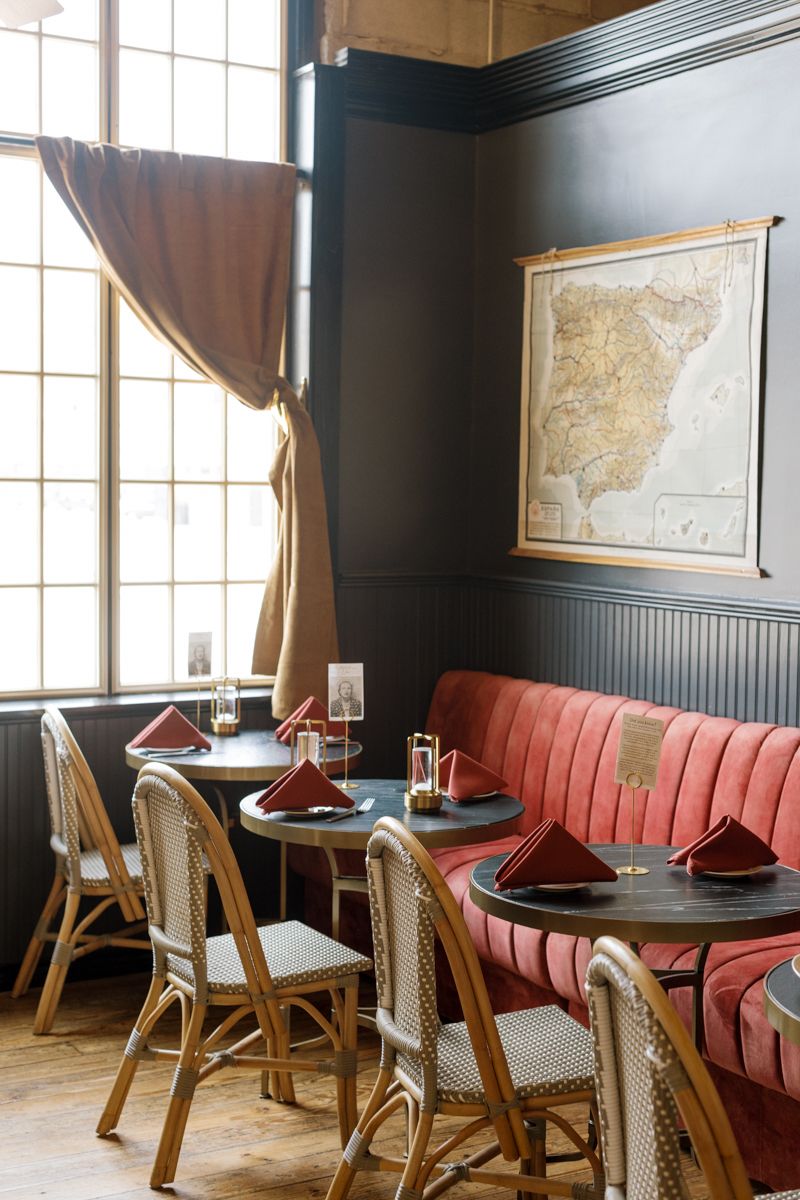 Cozy restaurant booth with red velvet banquette, rattan chairs, dark walls, and a vintage map above the seating area.