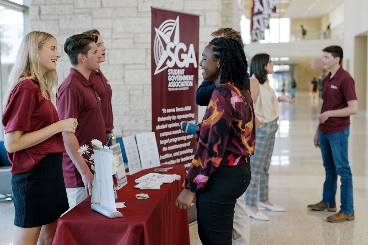 Students interact with an SGA Student Government Association booth in a university hallway.