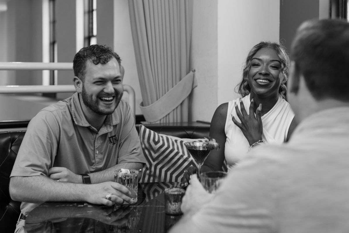 Two people laughing and enjoying drinks together at a bar table.