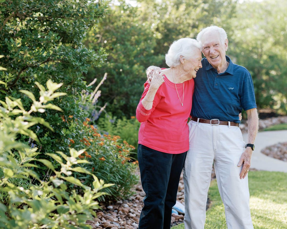 Happy elderly couple walking together in a lush garden, smiling and embracing on a sunny day.