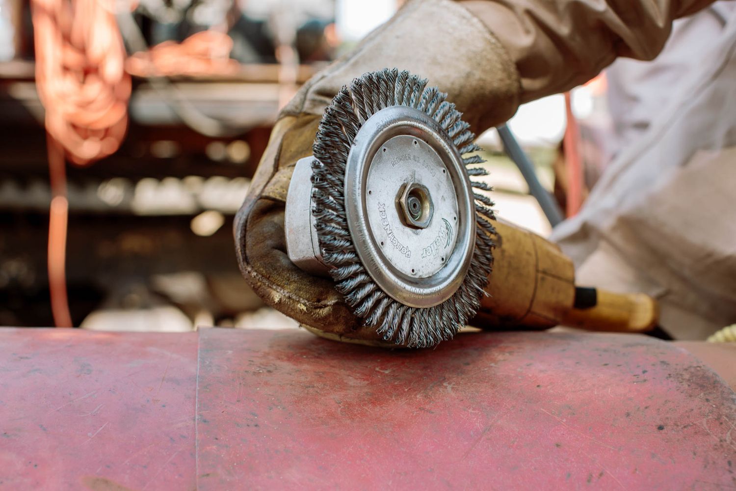 Worker using a wire wheel grinder on a metal pipe surface during industrial maintenance.