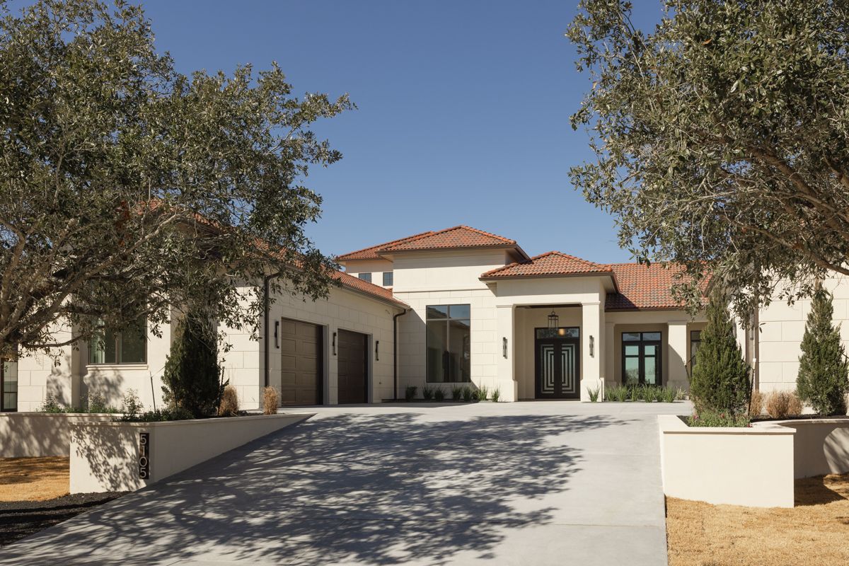 Modern Mediterranean-style home exterior with white stucco, terracotta roof, mature olive trees, and wide concrete driveway.