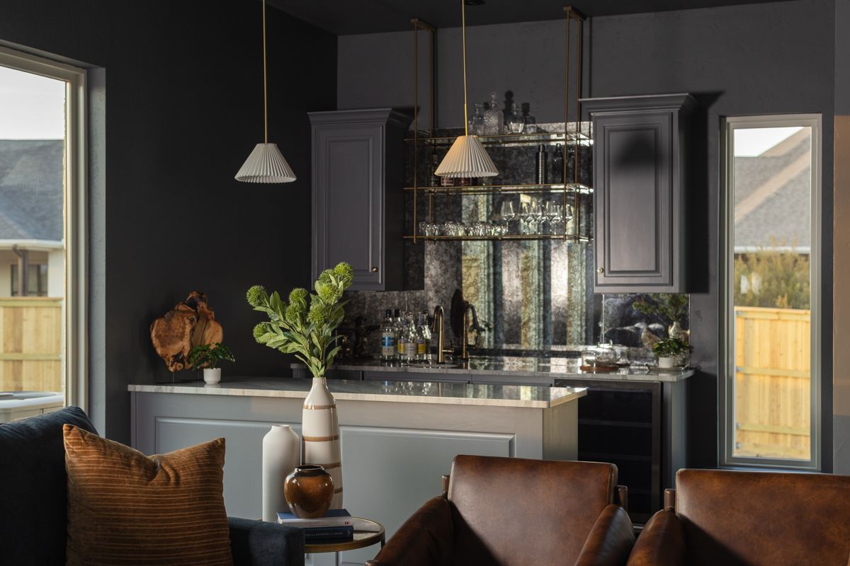 Moody dark bar area with charcoal walls, pendant lights, antique mirror backsplash, and leather seating.