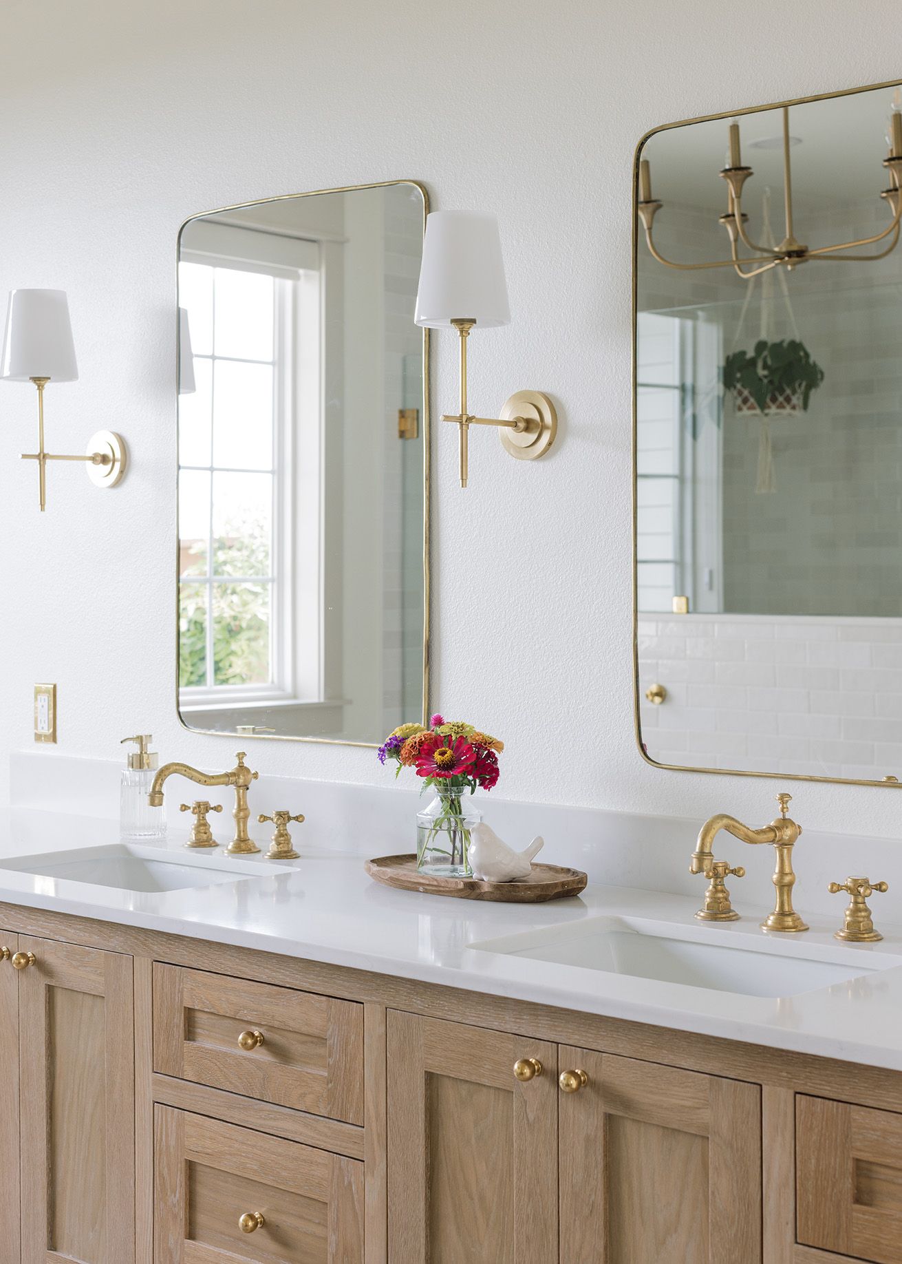 Double vanity bathroom with light wood cabinets, gold faucets, brass mirrors, and white sconces.