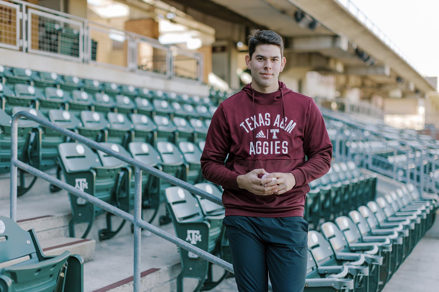 Young man in Texas A&M Aggies hoodie standing in stadium seating area.