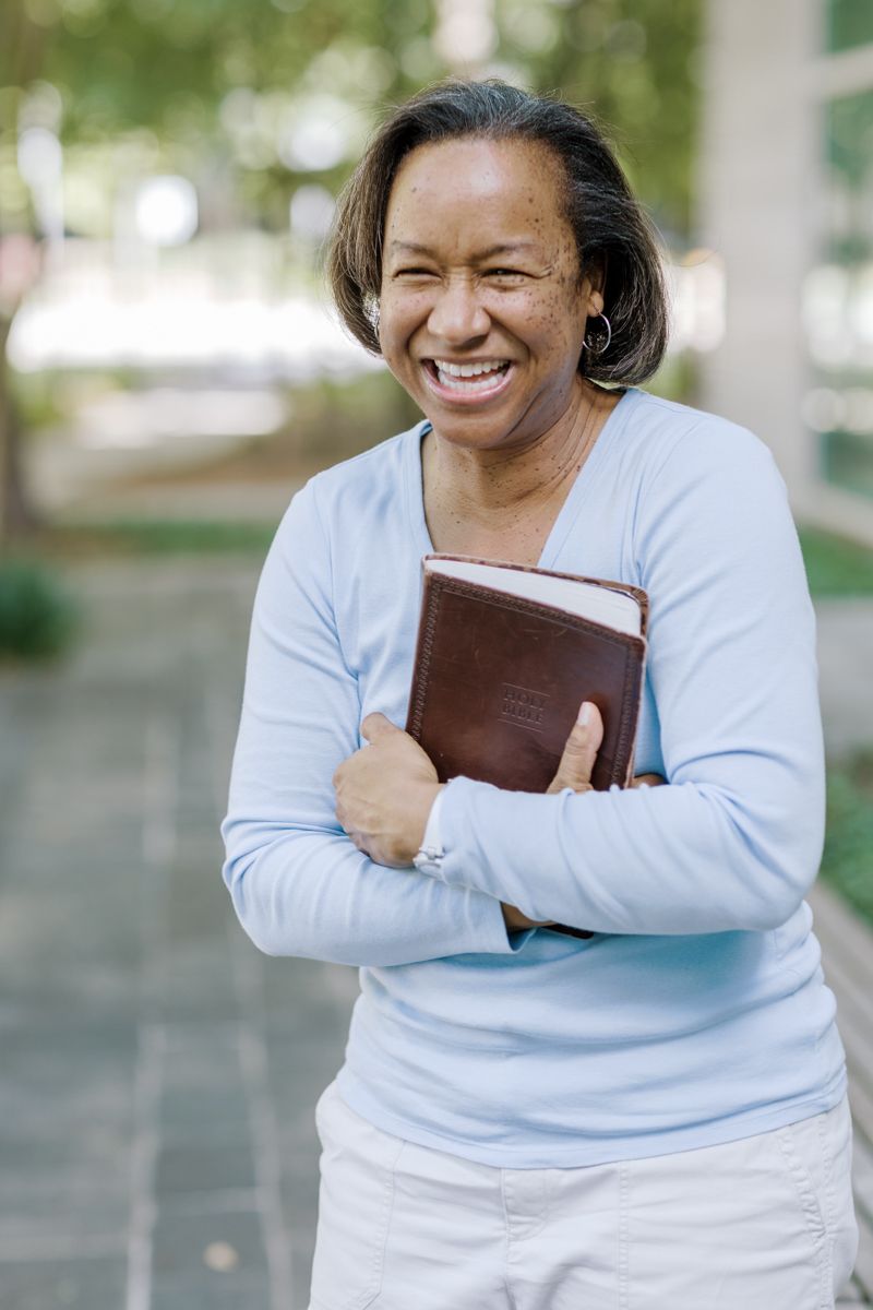 Smiling African American woman holding a brown leather Bible outdoors, wearing a light blue sweater.