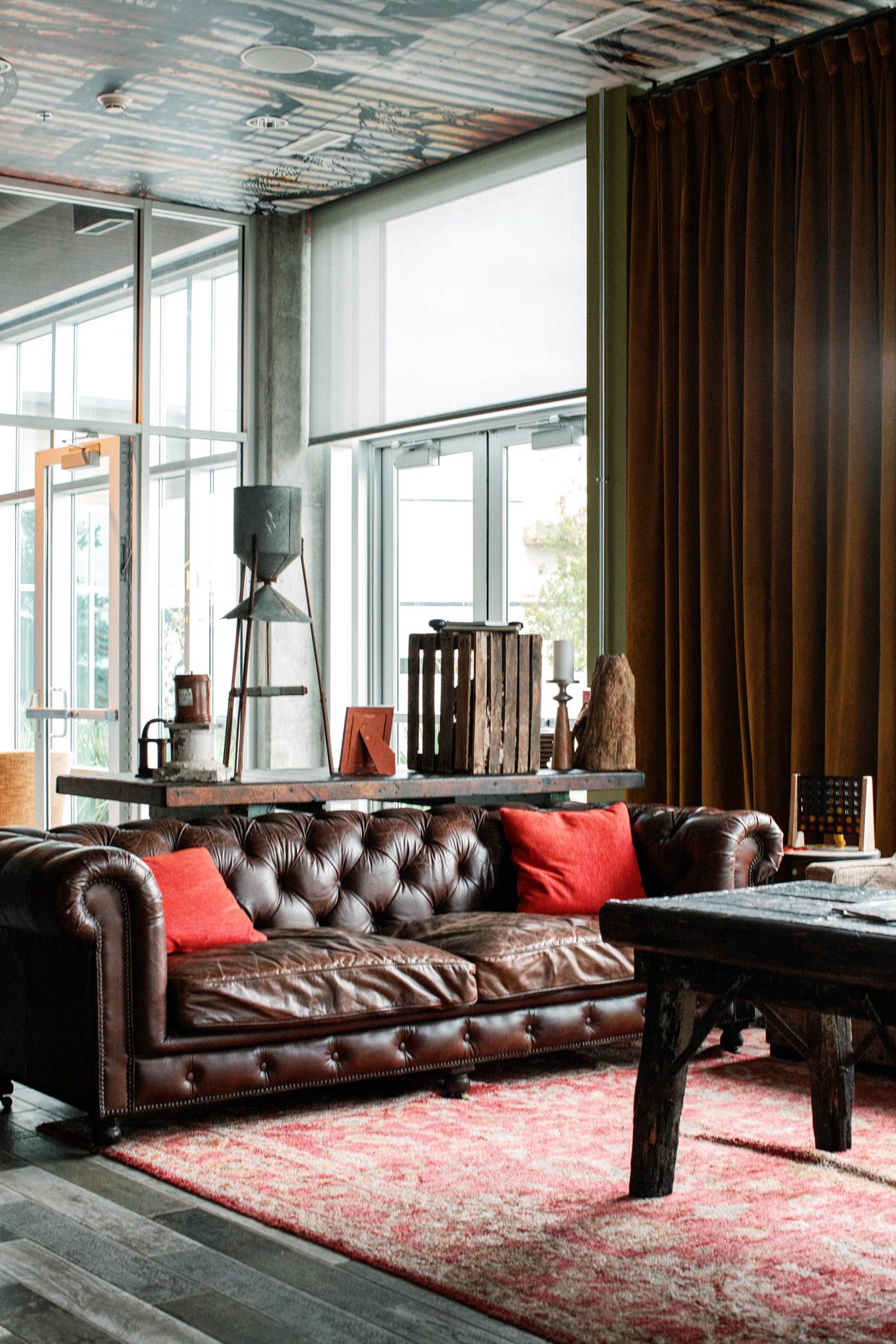 A luxurious tufted brown leather Chesterfield sofa with red pillows on a vintage rug in an industrial-style living room.