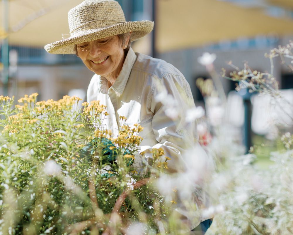 Smiling senior woman wearing a straw hat while tending to blooming plants outdoors.