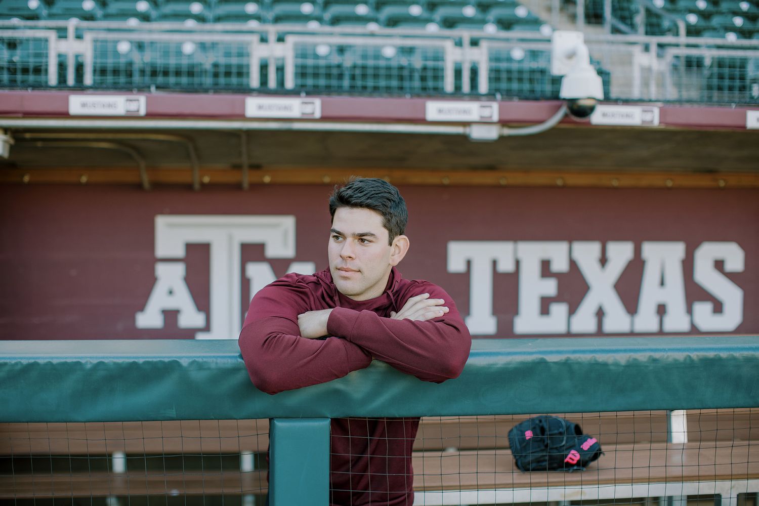 Texas A&M baseball player leaning on dugout railing at Aggie stadium.