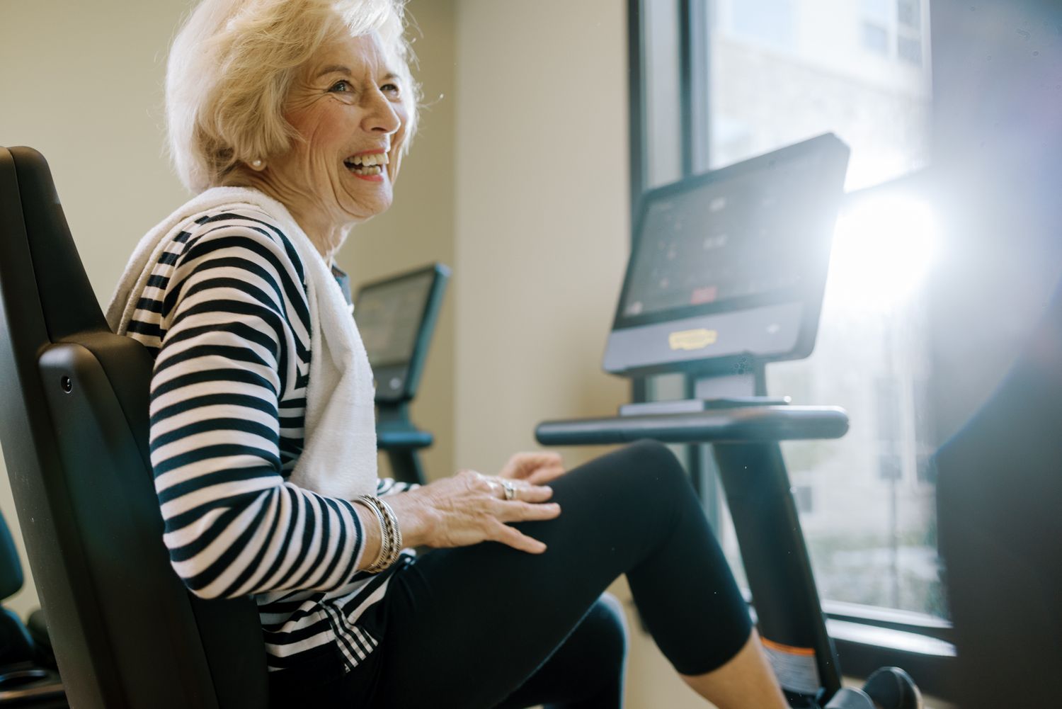 Smiling senior woman exercising on a recumbent bike at a modern gym, enjoying an active and healthy lifestyle.